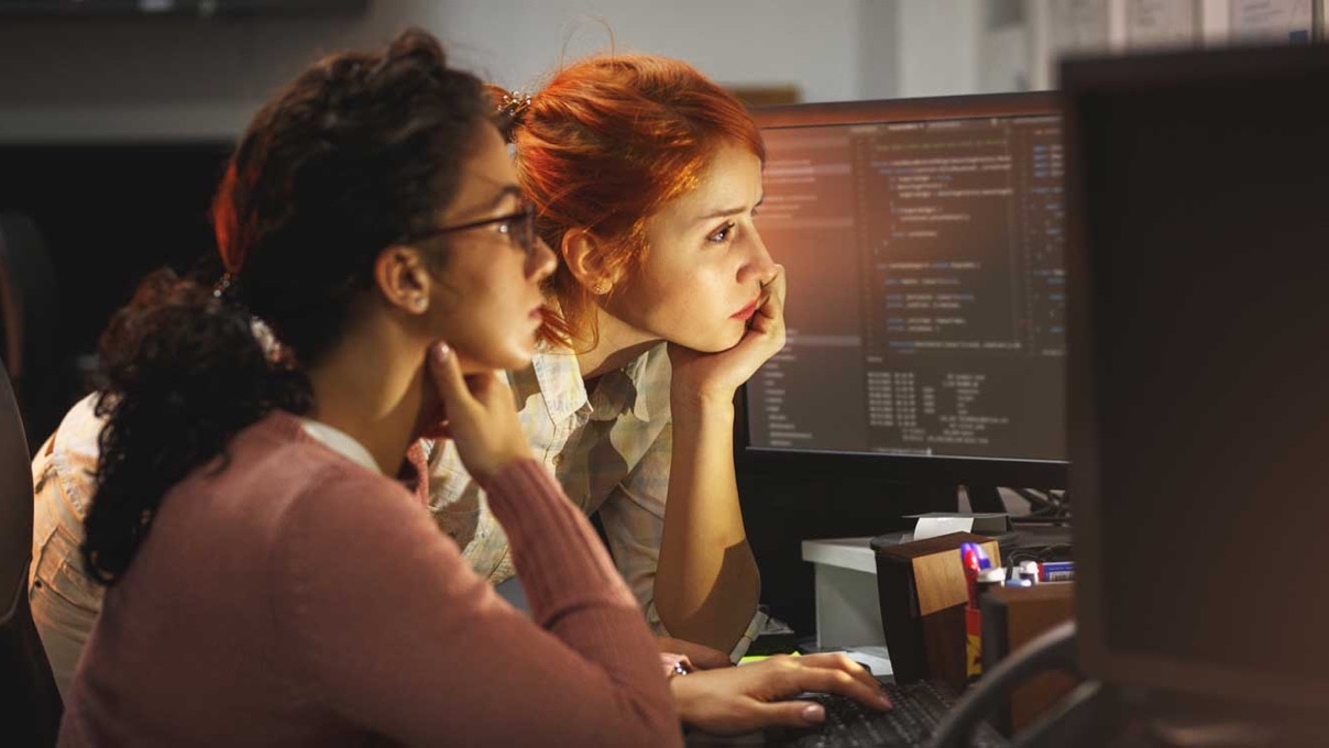 two young adult women working on computers with code-filled screens