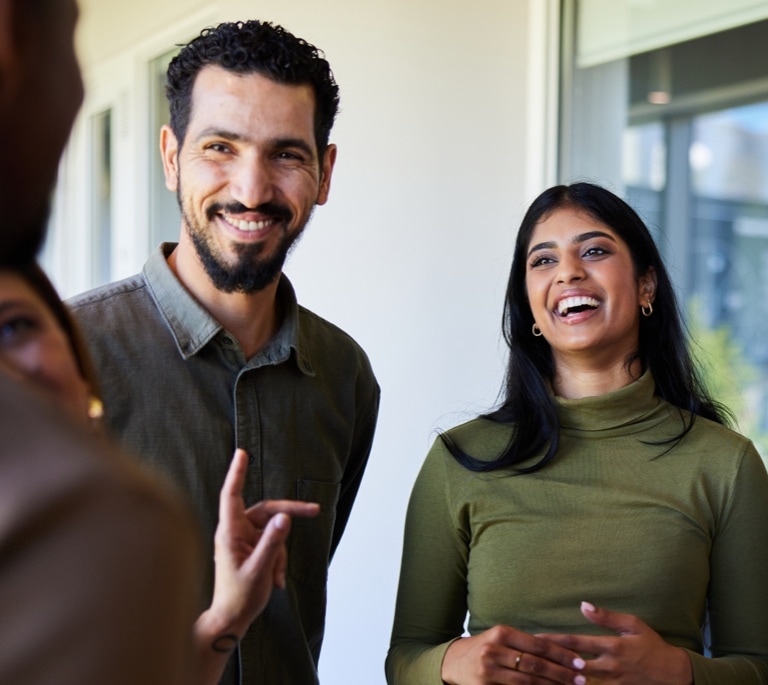 Young businesswoman laughing with a diverse group of coworkers while standing together in the corridor of an office