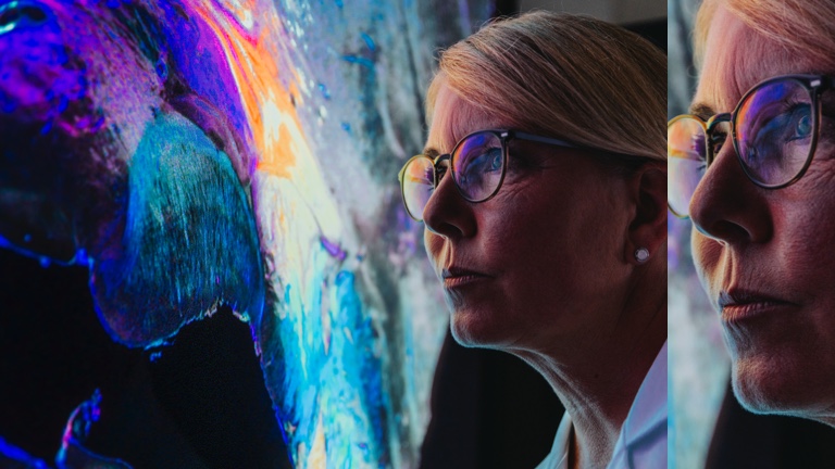 Middle-aged woman with glasses standing looking at large screen on the wall