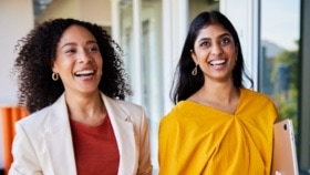 Diverse young businesswomen laughing together while walking in an office