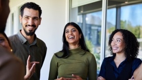 Young businesswoman laughing with a diverse group of coworkers while standing together in the corridor of an office