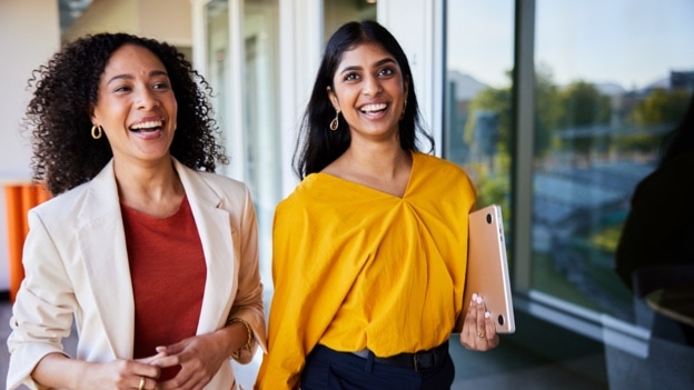 Diverse young businesswomen laughing together while walking in an office