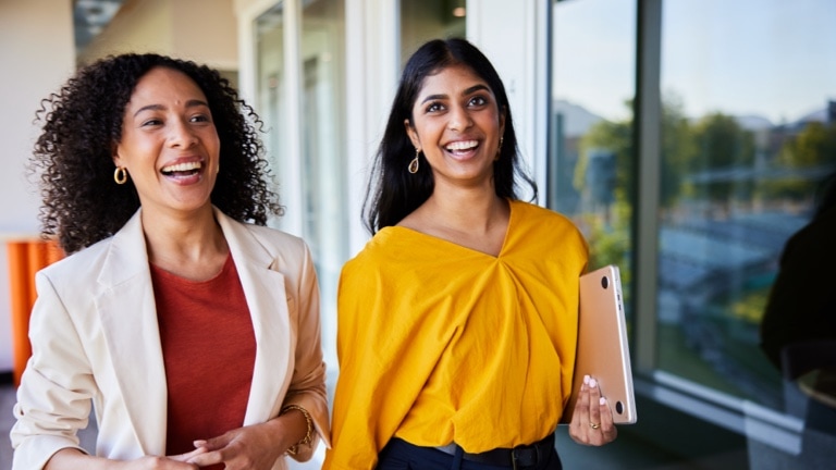 Diverse young businesswomen laughing together while walking in an office