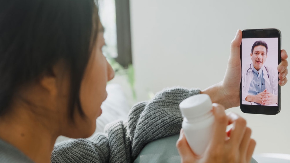 a woman with a mobile phone in her hand making a tele-consultation with a health care worker